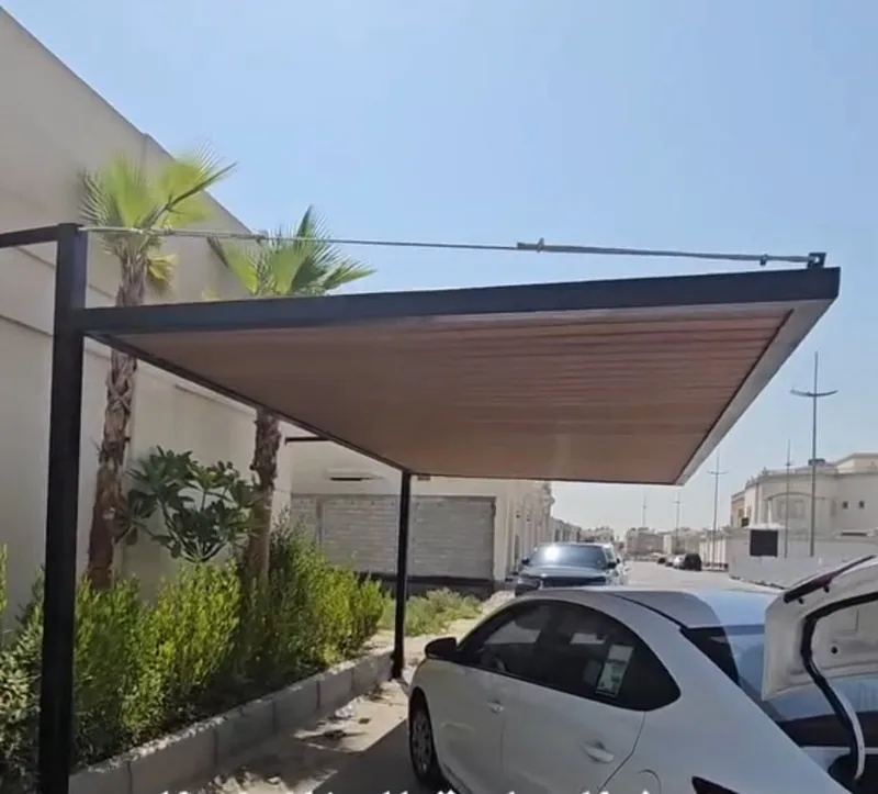 مظلة سيارات مسطحة بهيكل معدني داكن تغطي سيارة بيضاء بجانب رصيف