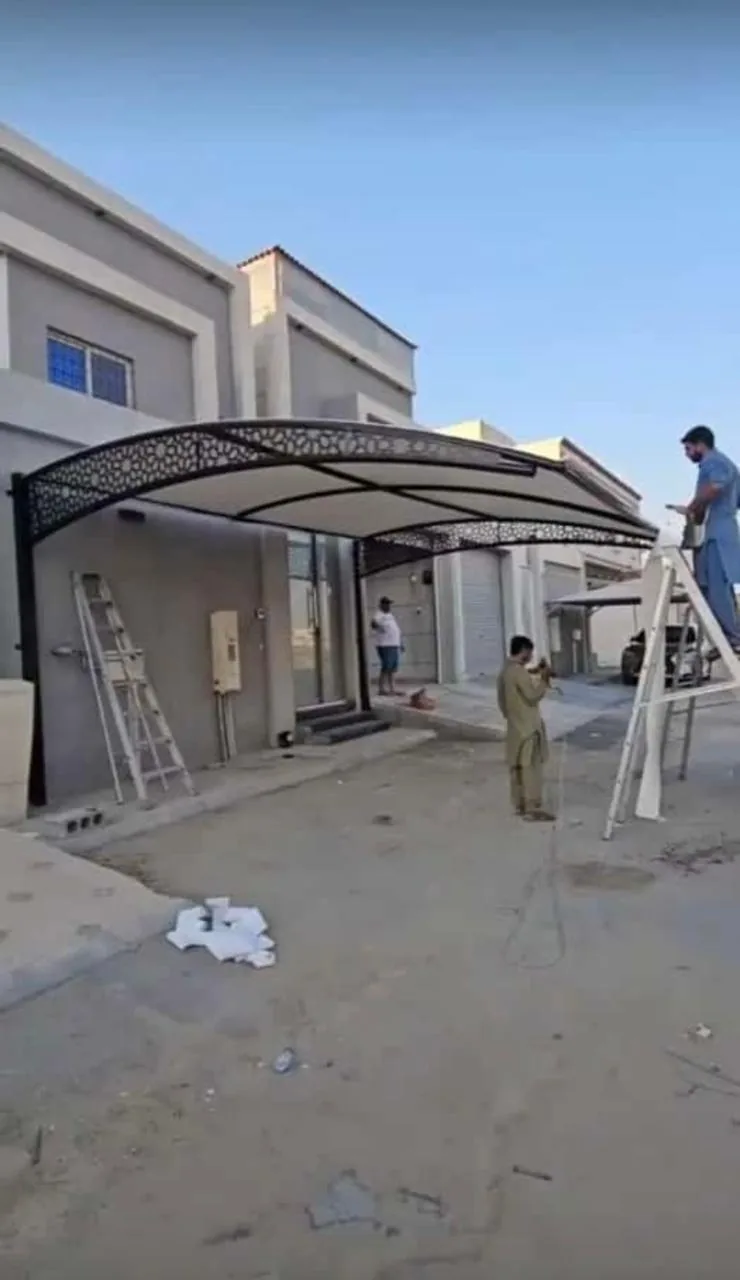 عاملان يركّبان مظلة سيارات معدنية أمام مبنى قيد الإنجاز