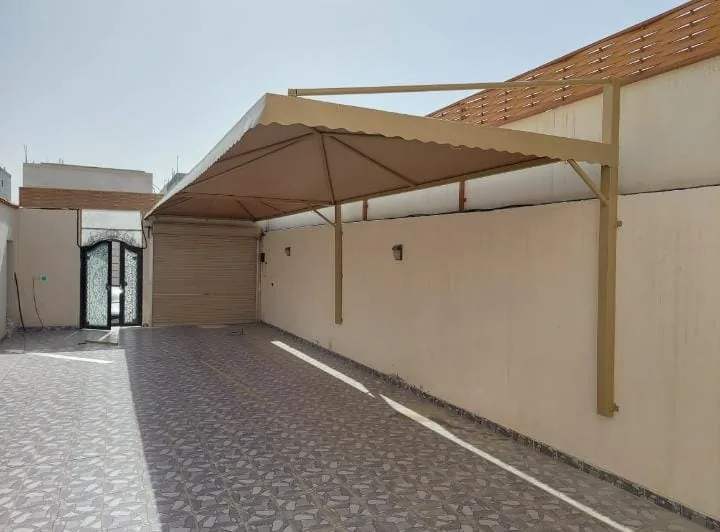 مظلة معدنية بلون بيج تغطي ممرًا ومواقف بمحاذاة جدار مبنى