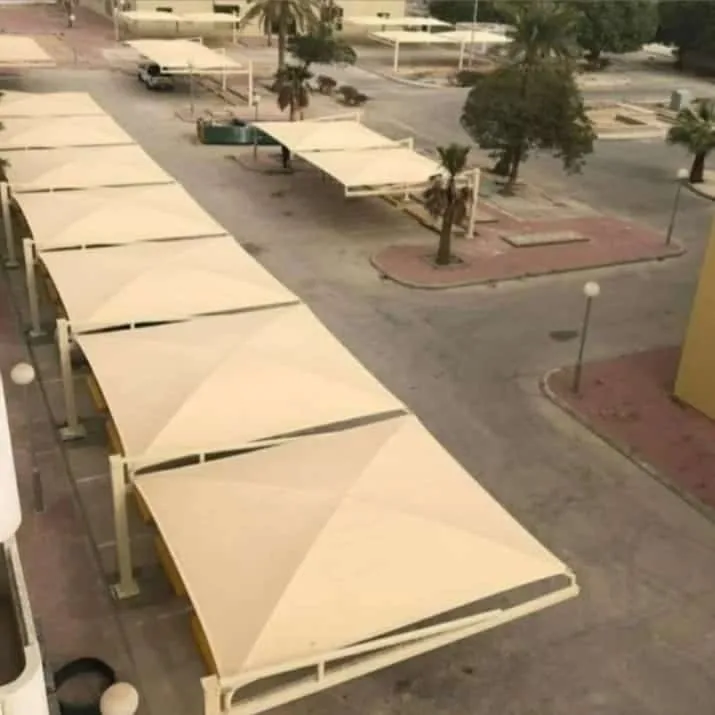 منظر علوي لصف طويل من مظلات مواقف السيارات بقماش فاتح بين أشجار النخيل
