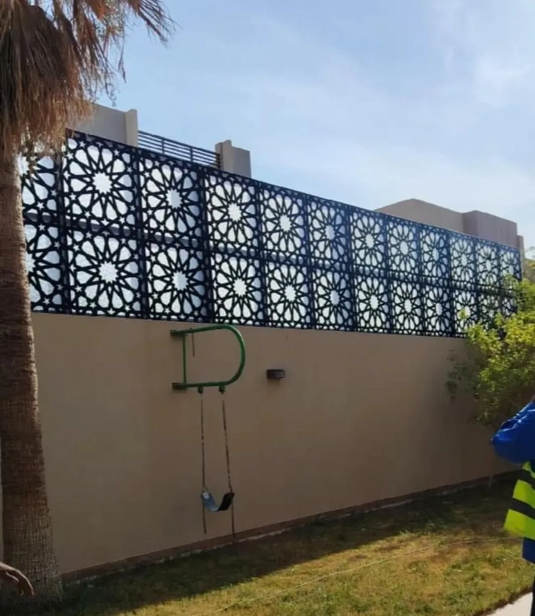 ألواح ساتر مزخرفة سوداء مثبتة أعلى سور حديقة بها شجرة نخيل