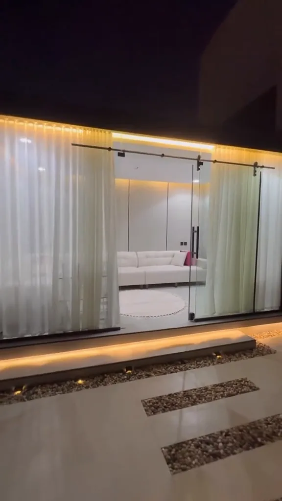 جلسة داخلية بأرائك بيضاء وستائر فاتحة داخل مجلس خارجي مكيّف