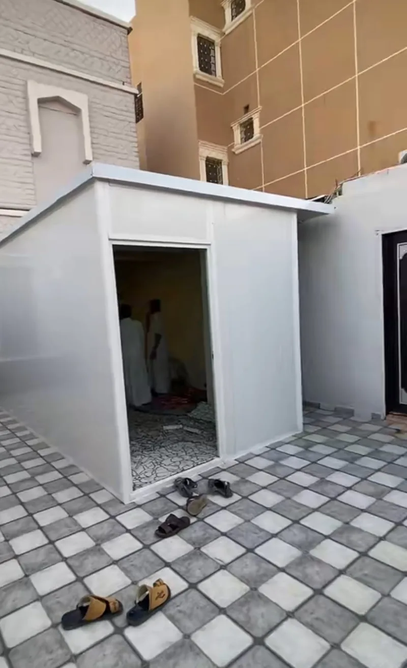 غرفة بجدران بيضاء وباب معدني داخل فناء منزل بأرضية بلاط مربعات
