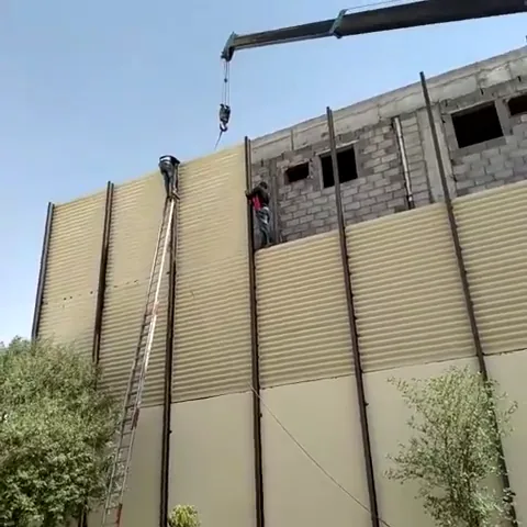 ونش يرفع لوحًا طويلًا من الساندوتش بانل لتثبيته على جدار مبنى قيد الإنشاء