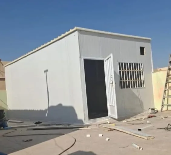 مبنى من ألواح الساندوتش بانل البيضاء بباب معدني ونوافذ شبكية في موقع مفتوح