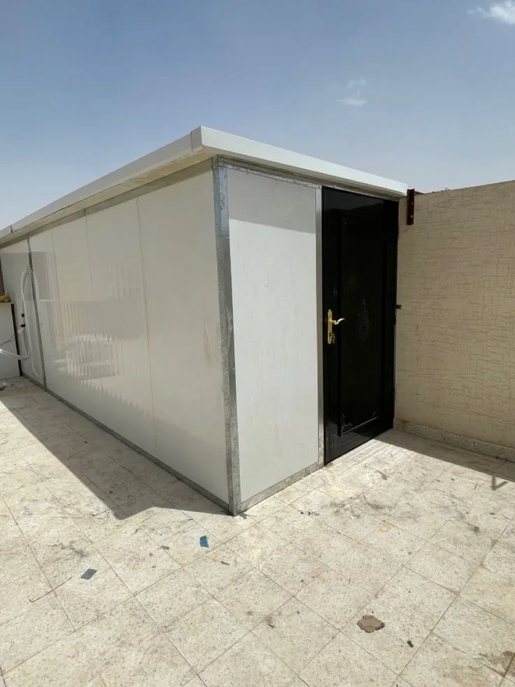 غرفة ساندوتش بانل بيضاء بباب معدني داكن مبنية على سطح منزل