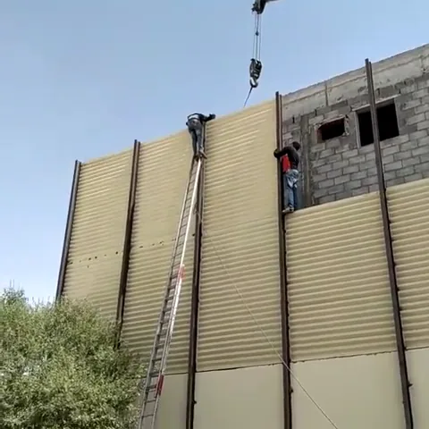 جدار مرتفع من ألواح الساندوتش بانل الرأسية بلون بيج أمام مبنى من البلوك