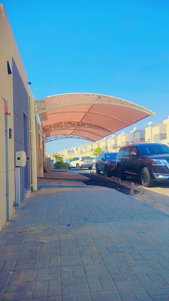 مظلة ممر منحنية بقماش فاتح تغطي رصيفًا بمحاذاة مبنى